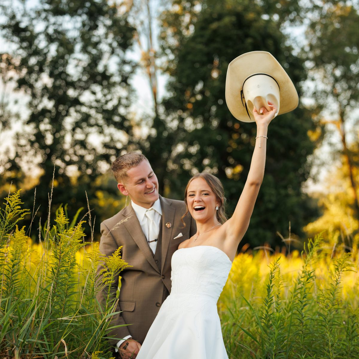 A bride laughing as she lifts the groom's cowboy hat into the air