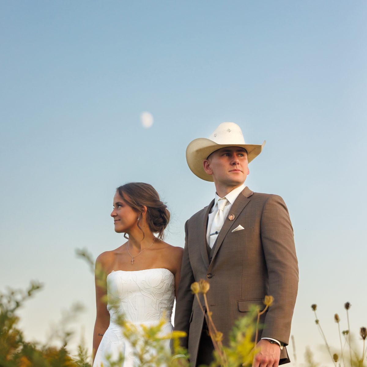 A bride and groom in a wildflower meadow under a daytime moon