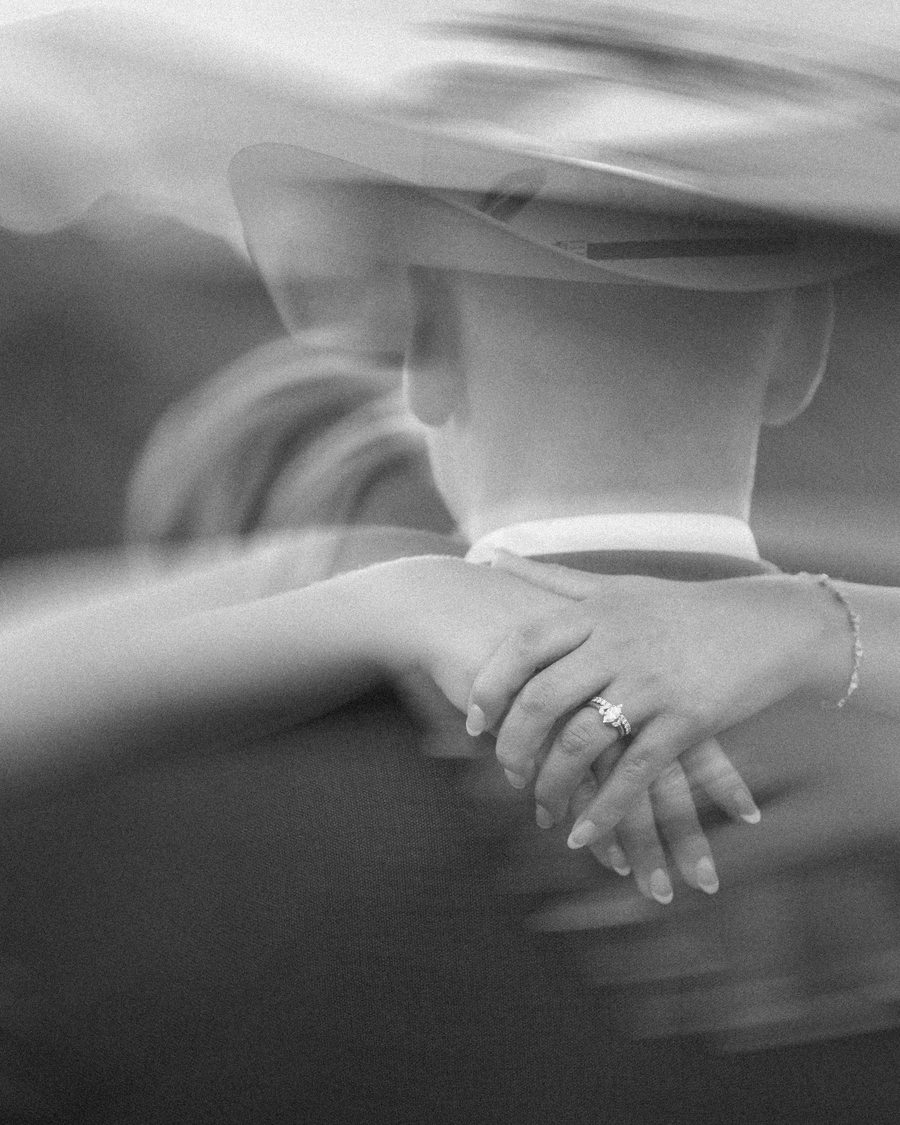 A close black and white photograph of the couple's hands and rings