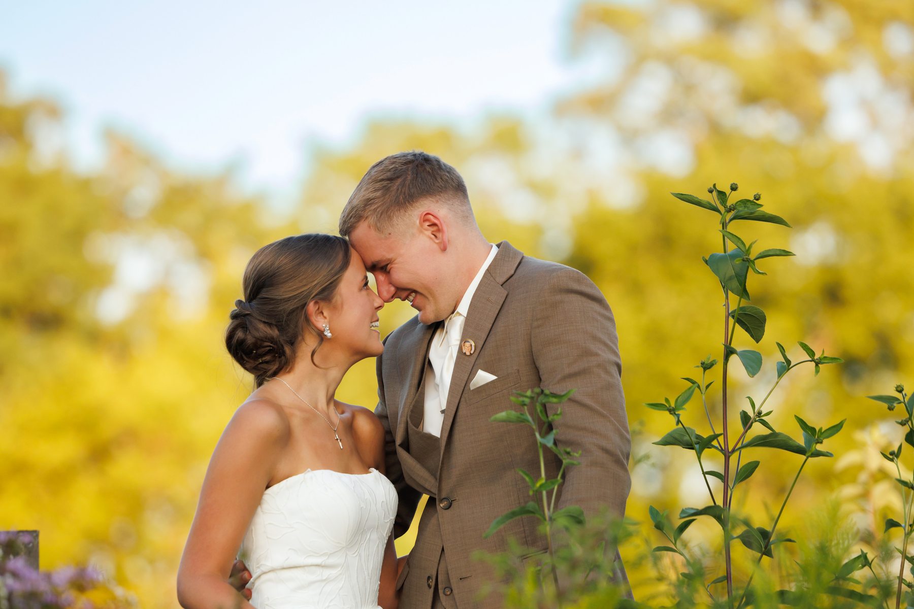 A bride and groom with their foreheads together in golden evening light